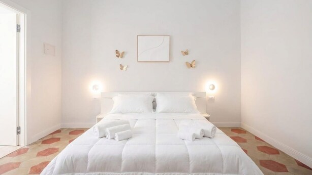 Ein Hotelzimmer mit einem Bett, weißer Bettwäsche, einem gerahmten Bild an der Wand und einer Tür links.