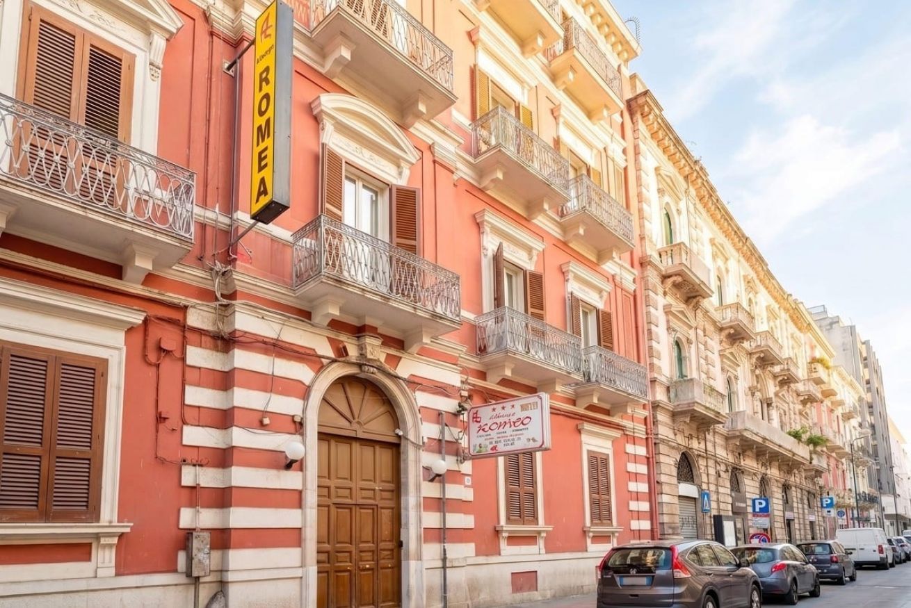 A building with a prominent 'ROMEA' sign, a large wooden door, and multiple balconies with metal railings.