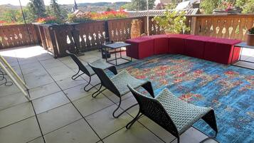 Een terras met betegelde vloer, een rode, beklede bank en twee rieten stoelen.
