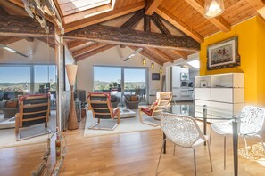 A spacious living area with a high ceiling, large windows, and a view of the landscape.