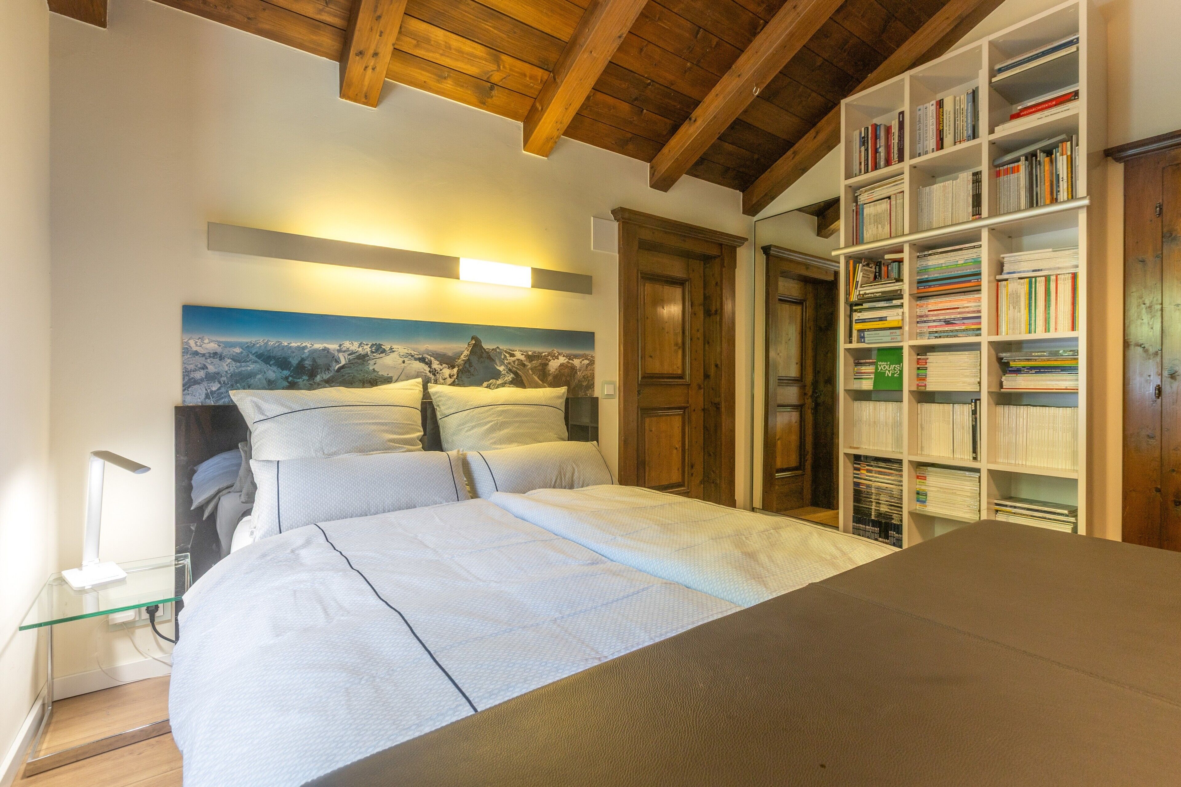 Een slaapkamer met een bed, een boekenkast en een schilderij aan de muur.