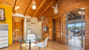 A modern interior with wooden beams, a glass table, white chairs, and a view through a glass door. - Apartment "Weiser Hirsch" in Chalet Burgblick with Castle Views and Modern Comfort (Weilrod)