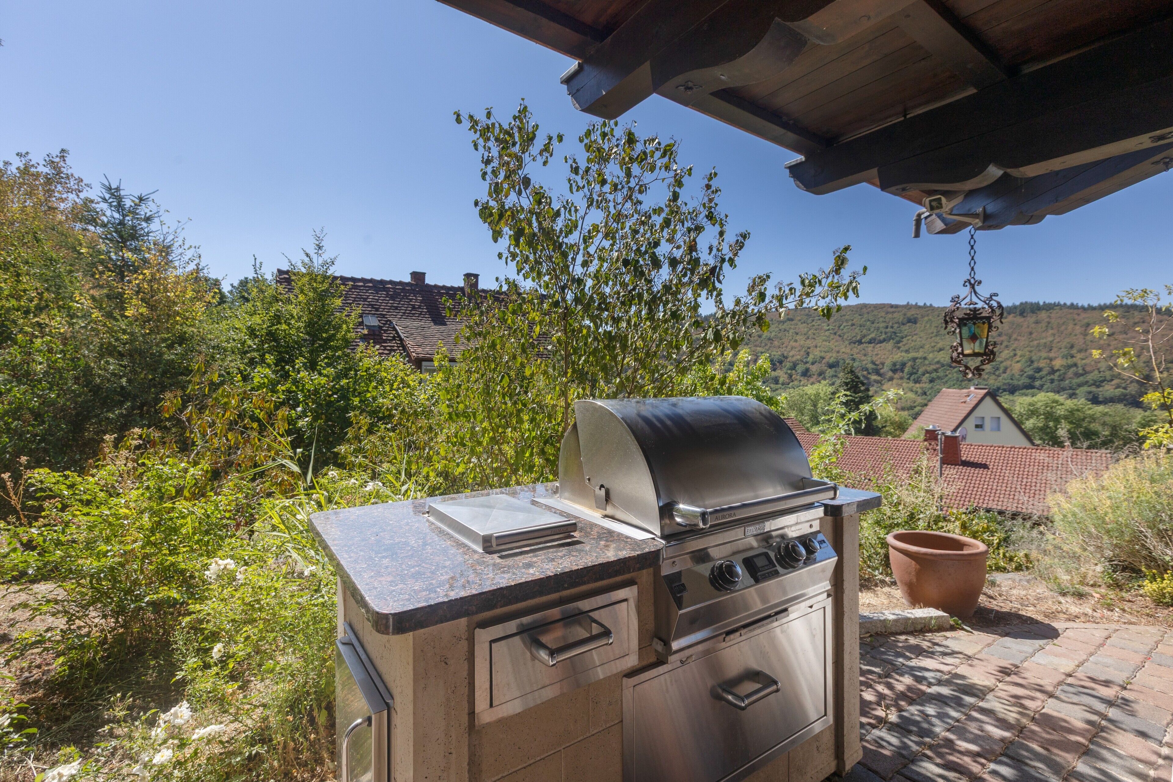 An outdoor grill with a digital display, surrounded by greenery and a view of a hilly landscape.