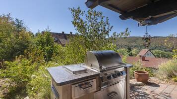 An outdoor grill with a digital display, surrounded by greenery and a view of a hilly landscape.