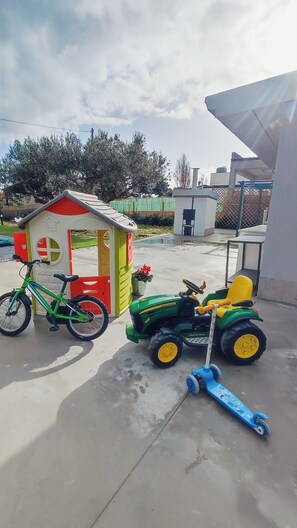 A concrete patio with a small playhouse, a green bicycle, a toy John Deere tractor, and a blue toy shovel. - Villa du Cori: Pool and Relaxation (Alcamo)