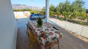 A balcony with a table set for dining, a car parked outside, and a view of a vineyard and mountains. - Villa du Cori: Pool and Relaxation (Alcamo)