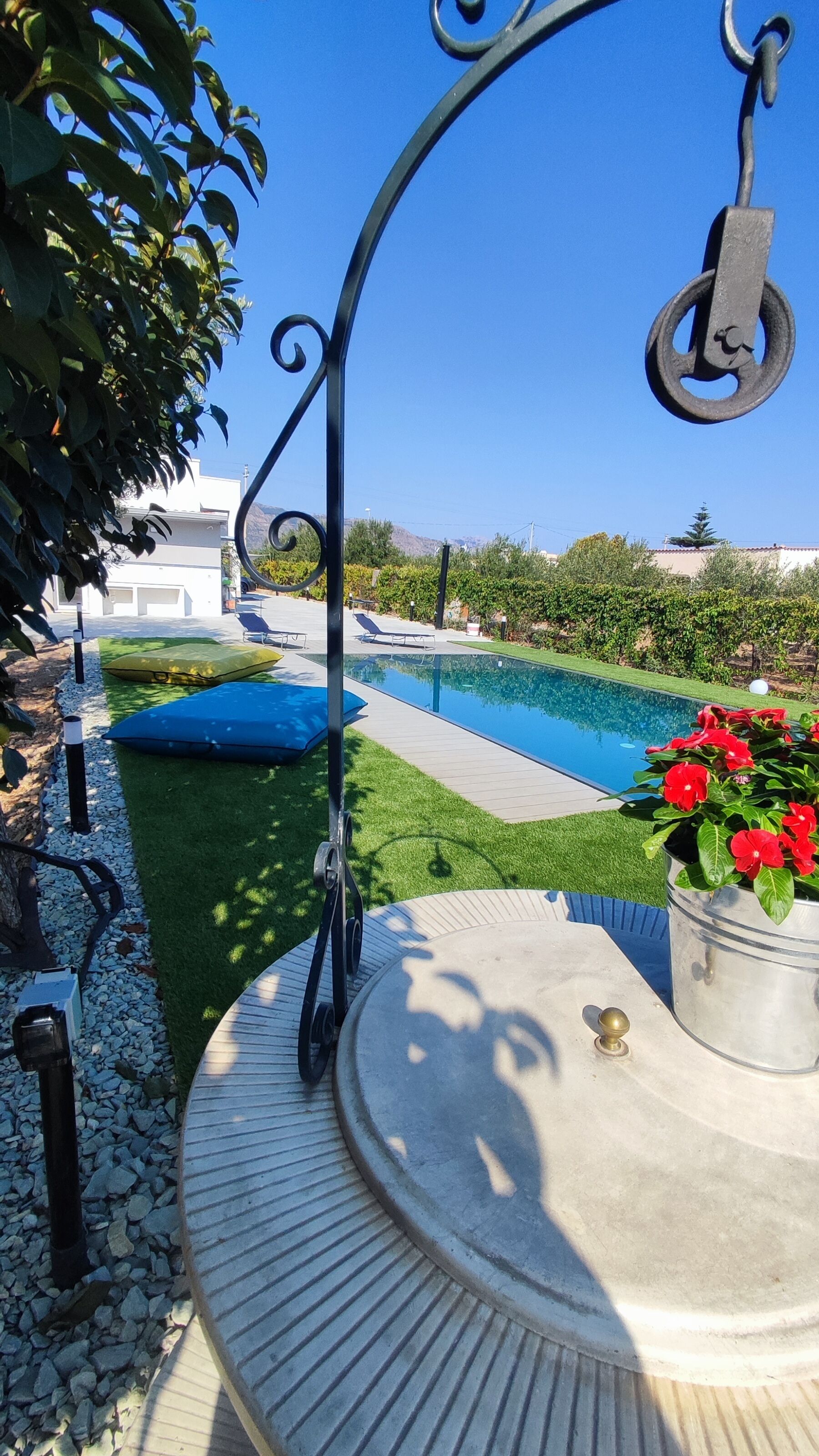 A pool area with a clear blue sky, a white building in the background, and a table with a potted plant.