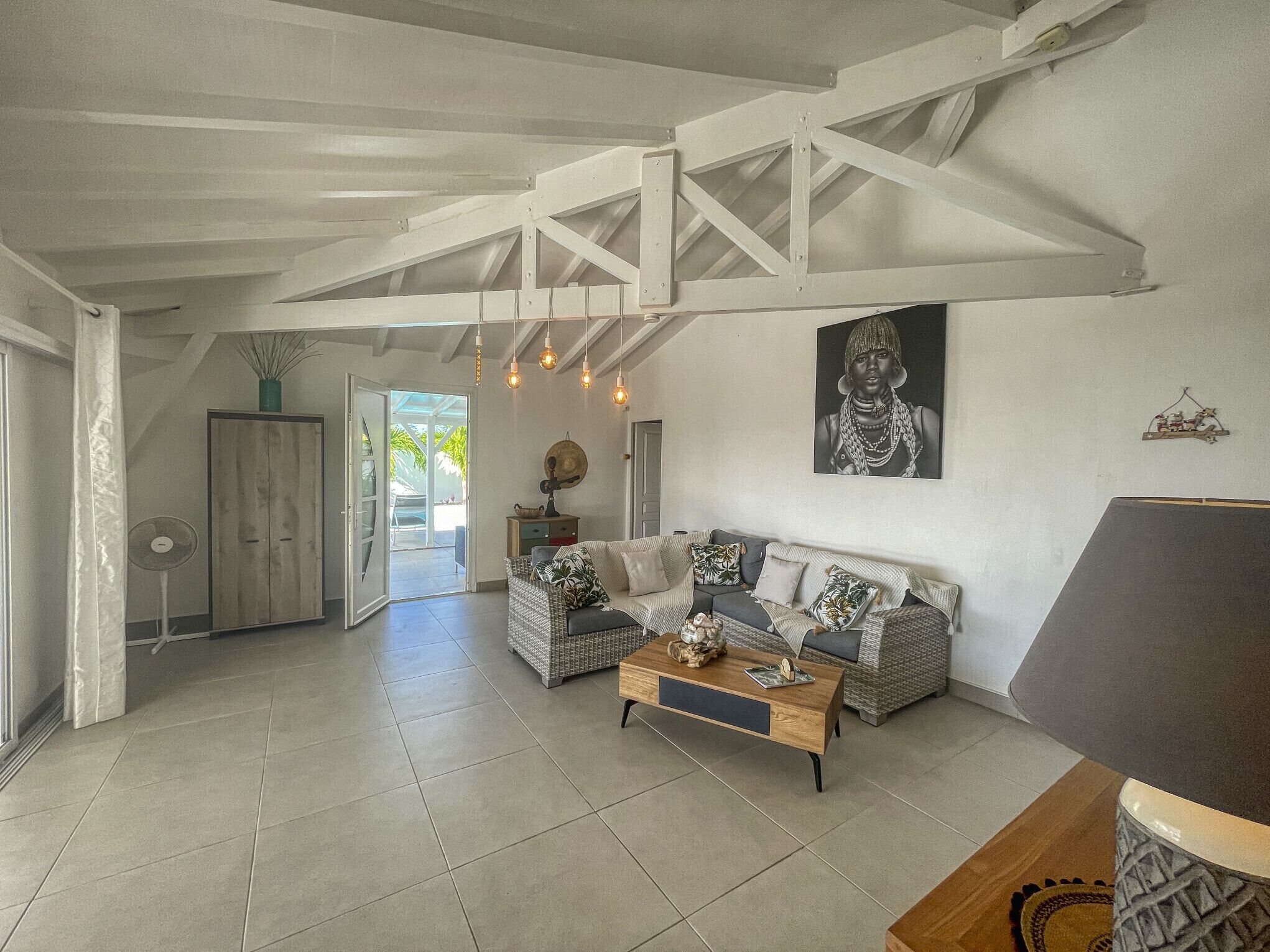 A spacious living area with a high ceiling, a sofa set, a coffee table, and a fan.