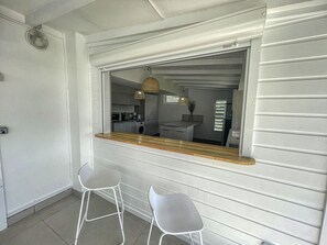 Ein Zimmer mit einer Küchenzeile, zwei Barhocker und einem Fenster mit Blick zur Küche.