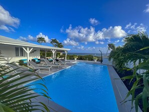 A swimming pool with lounge chairs and a covered area, surrounded by palm trees and a clear sky. - 800m beach - Villa pool & spa - 6 ad + 1 child (Saint-François)