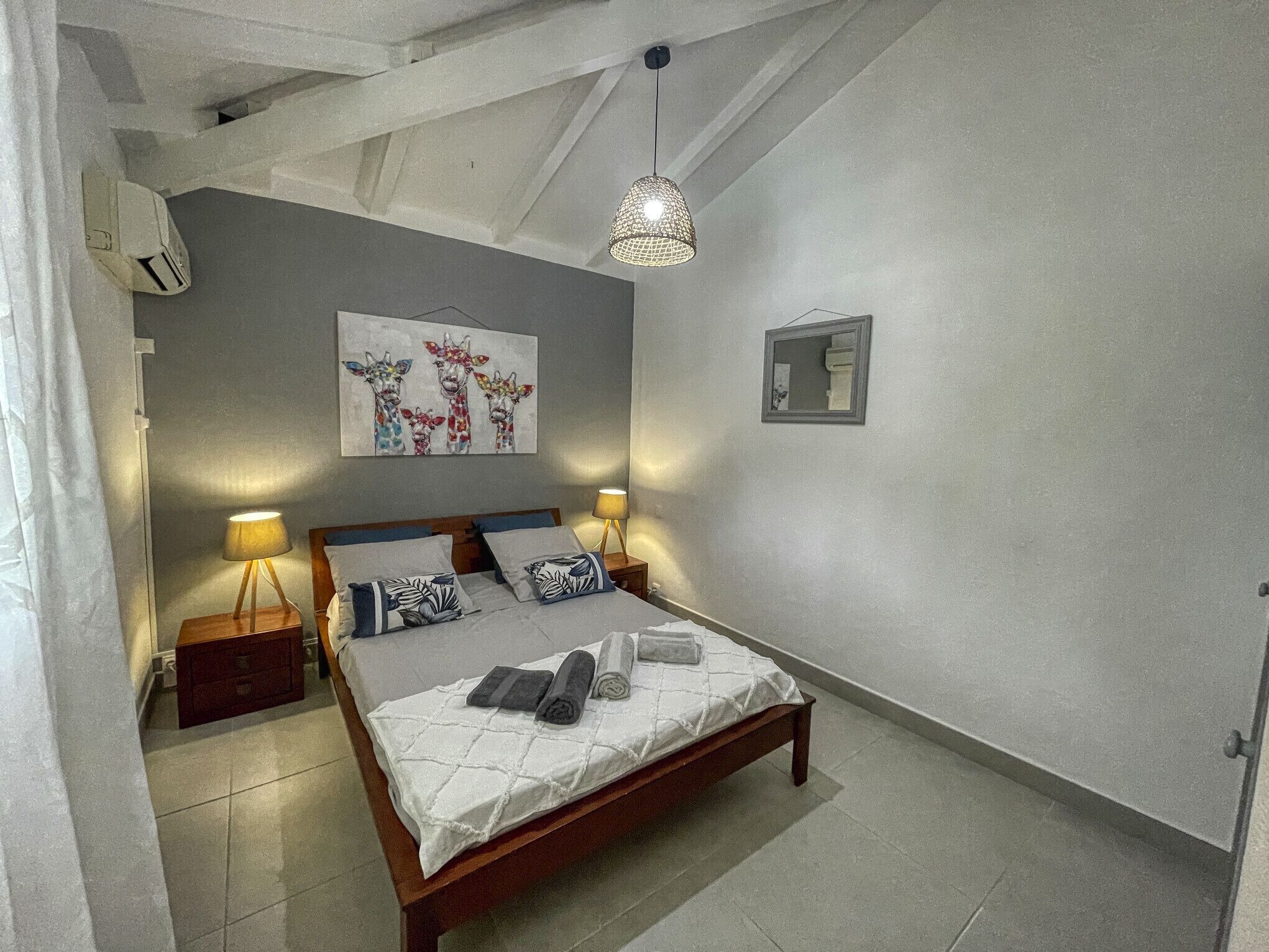 Ein Schlafzimmer mit einem Bett, zwei Nachttischen, einer Hängeleuchte, einem Wandspiegel und einem Gemälde.