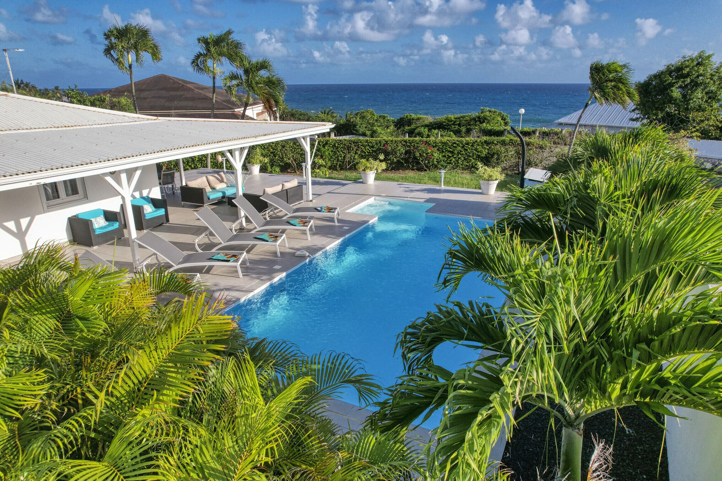 A pool area with lounge chairs and a covered seating area, surrounded by tropical plants.