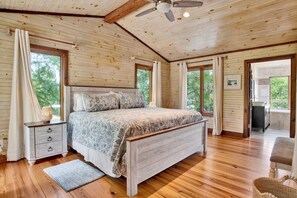 Une chambre à coucher avec un plafond en bois, un lit avec une literie à motifs, une table de chevet et une fenêtre avec des rideaux.