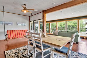 Un espace repas avec une table en bois, des chaises blanches et un ventilateur de plafond.
