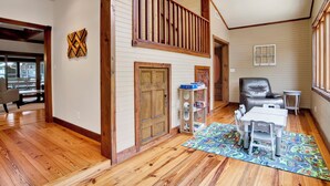 A spacious room with wooden flooring, a loft area with a railing, a door, a chair, a small table, and a colorful rug. - "Catican Bayou" Fish River Waterfront Home 3 bedrooms; 5 bathrooms  Kayaks (Summerdale)