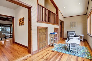 A spacious room with wooden flooring, a loft area with a railing, a door, a chair, a small table, and a colorful rug. - "Catican Bayou" Fish River Waterfront Home 3 bedrooms; 5 bathrooms  Kayaks (Summerdale)