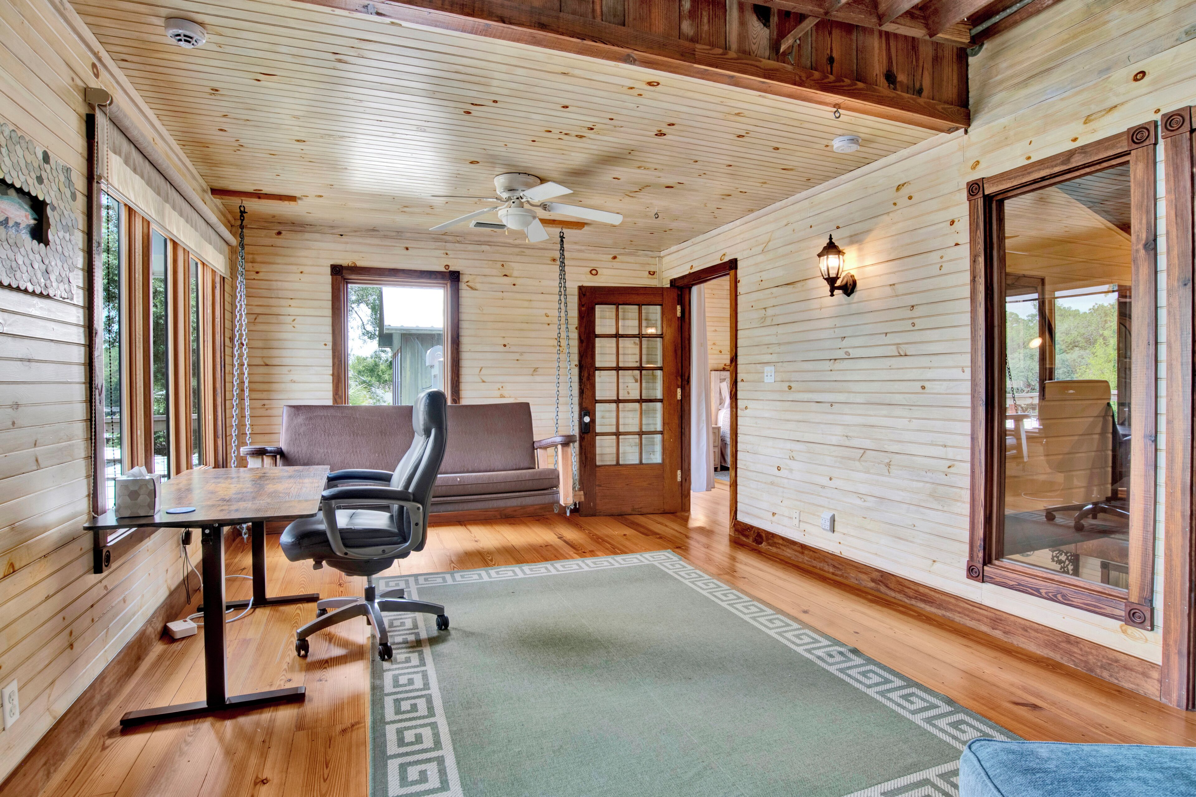 Un intérieur en bois comprenant un bureau, une chaise, un canapé et un ventilateur de plafond.