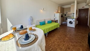 Un espacio habitable compacto con kitchenette, una zona de comedor con productos para el desayuno, y una cama con una manta verde.