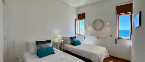 A room with two beds, a small table, a mirror, and a window with a view.