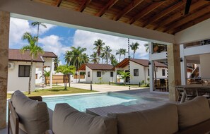 Zona junto a la piscina con mobiliario exterior, vista a un barrio residencial y cielo despejado.