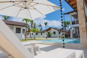 A poolside area with a white umbrella, lounge chairs, and a clear view of a swimming pool. - Charming 1-bedroom bungalow with AC in Las Terrenas (Las Terrenas)