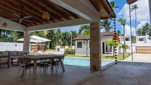 Uma área externa coberta com piscina, mesa de jantar, cadeiras e guarda-sóis.