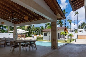 Ein überdachter Außenbereich mit Pool, Esstisch, Stühlen und Sonnenschirmen.