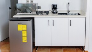 Uma cozinha compacta com geladeira, micro-ondas, cafeteira e uma pia pequena.