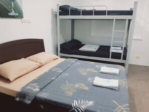 Una cama litera con una cama inferior y un catre superior. Hay una cama a la izquierda con cabecera y almohadas.