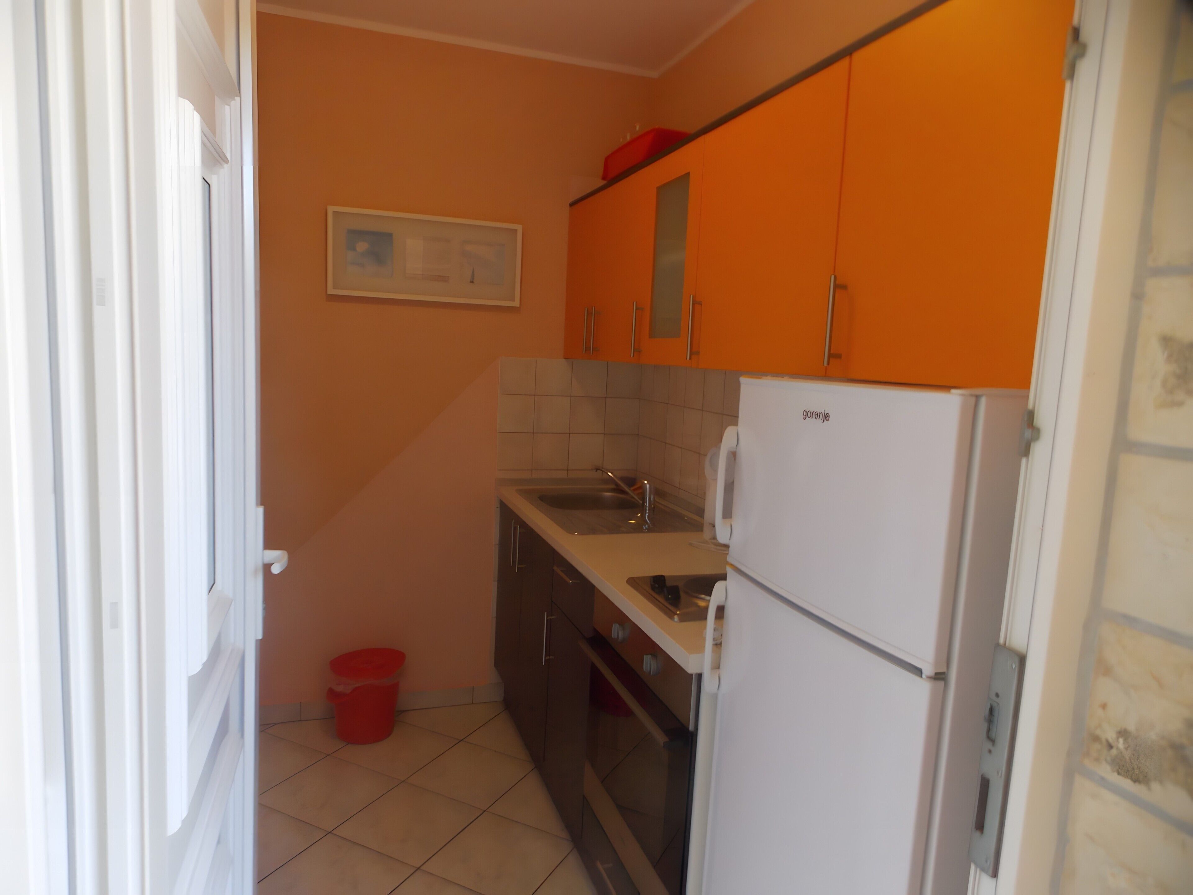 Een kleine keuken met oranje kastjes, een witte koelkast en een betegelde achterwand.