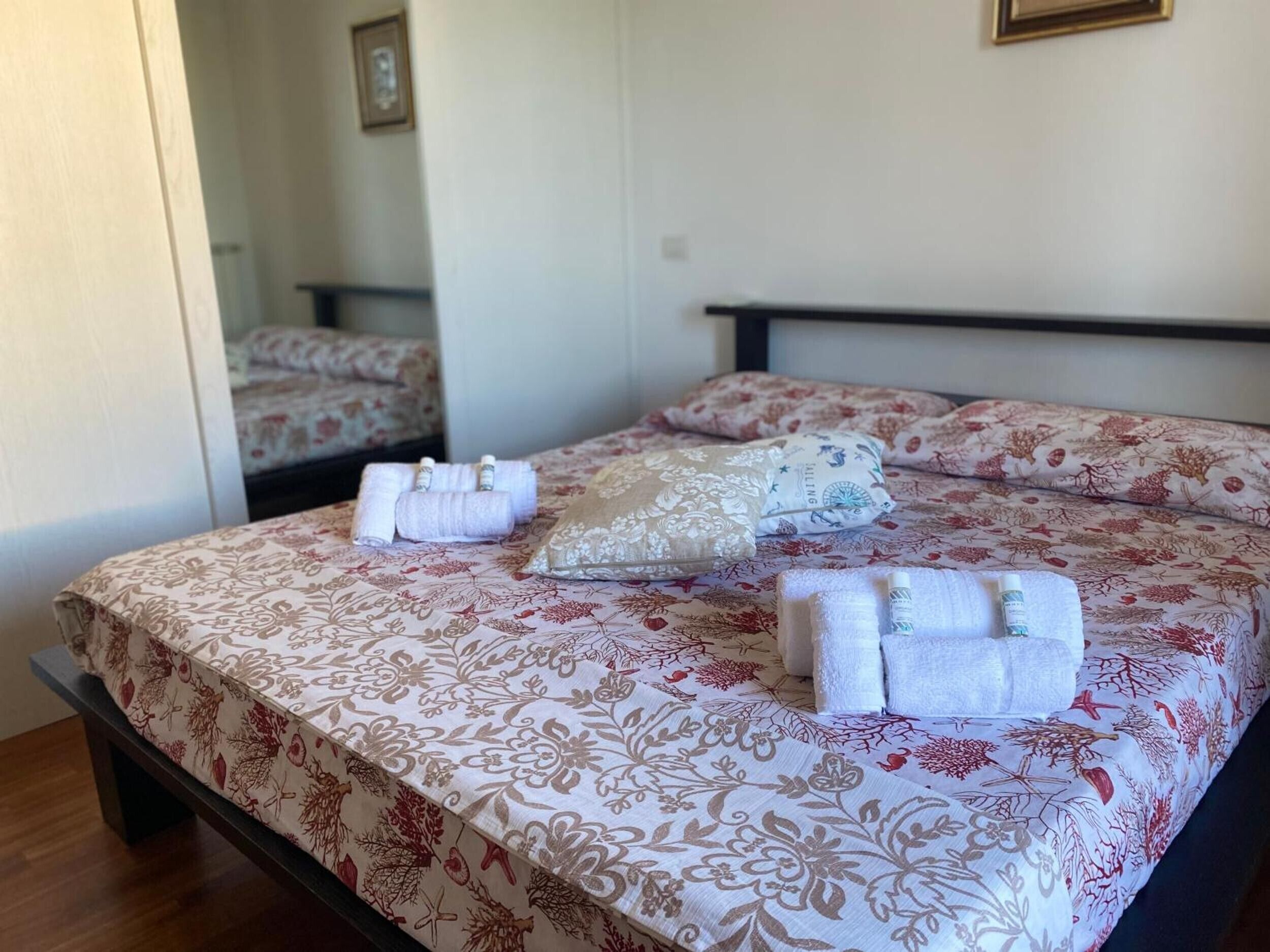 Un lit avec une literie à motifs floraux, une table de chevet et un miroir qui reflète la pièce.