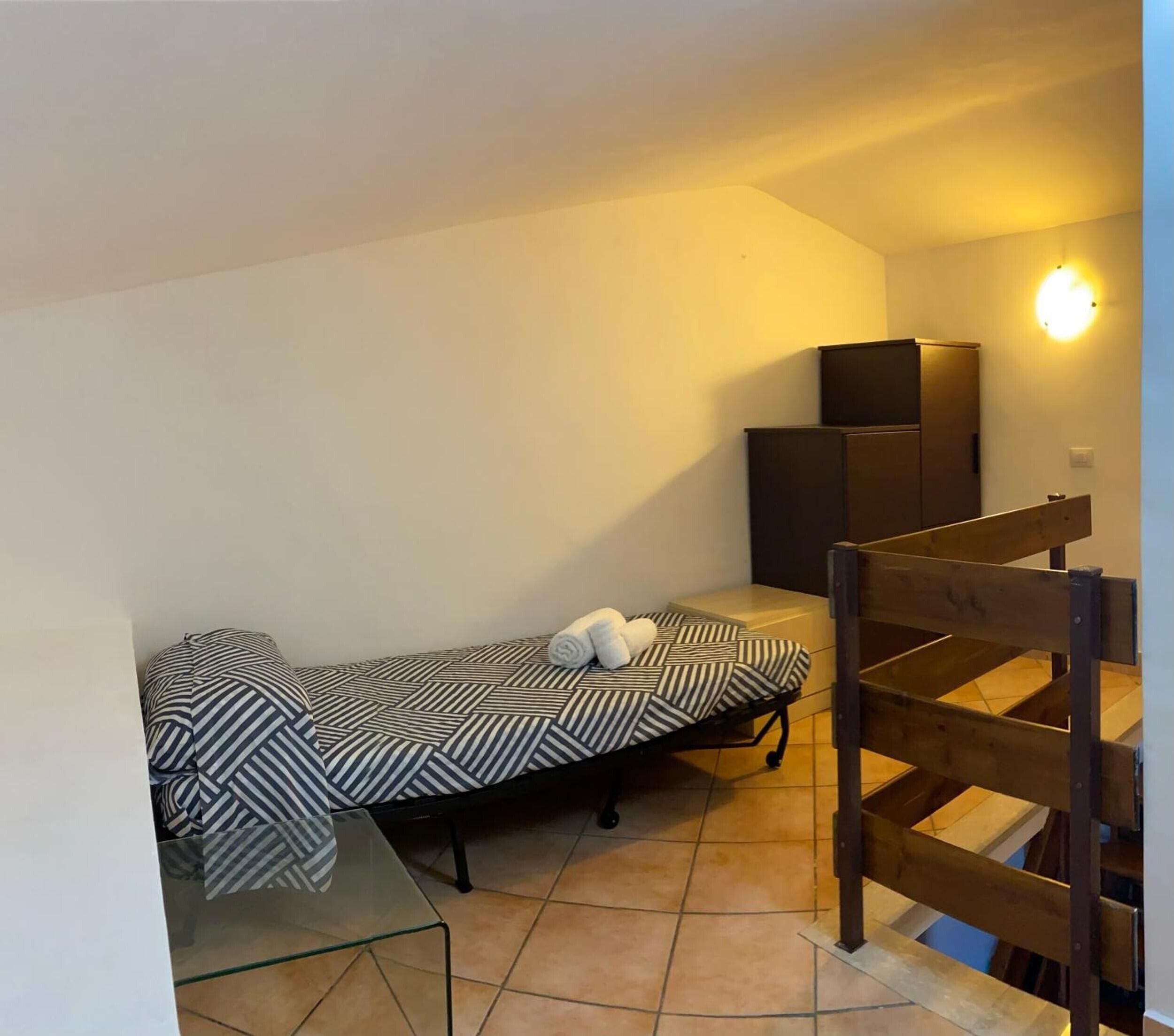 Une petite pièce, de taille modeste, comprenant un lit simple, une chaise en bois et un petit meuble.
