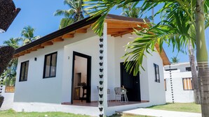 Um edifício térreo com telhado plano, varanda coberta com duas cadeiras e porta que dá para o interior.