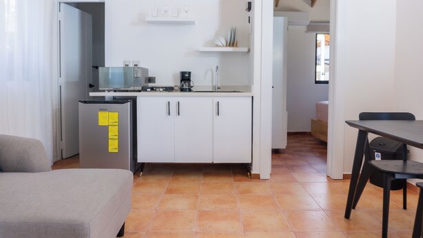 Cozinha compacta com geladeira, micro-ondas e cafeteira. Há uma área de jantar com mesa e cadeiras.