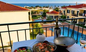 Ein Balkon mit Tisch, gedeckt für eine Mahlzeit, mit Blick auf einen Pool und die Küste.
