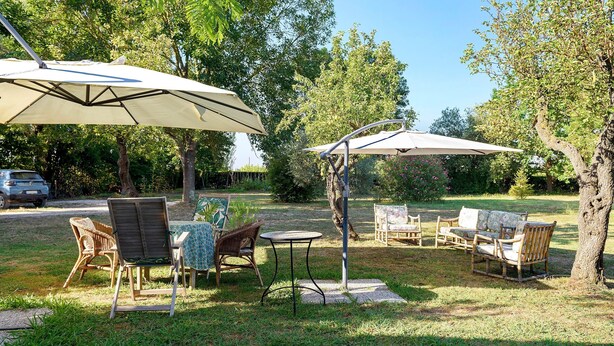 Un'area salotto all'aperto con tavoli e sedie, circondata da alberi e un'auto sullo sfondo.