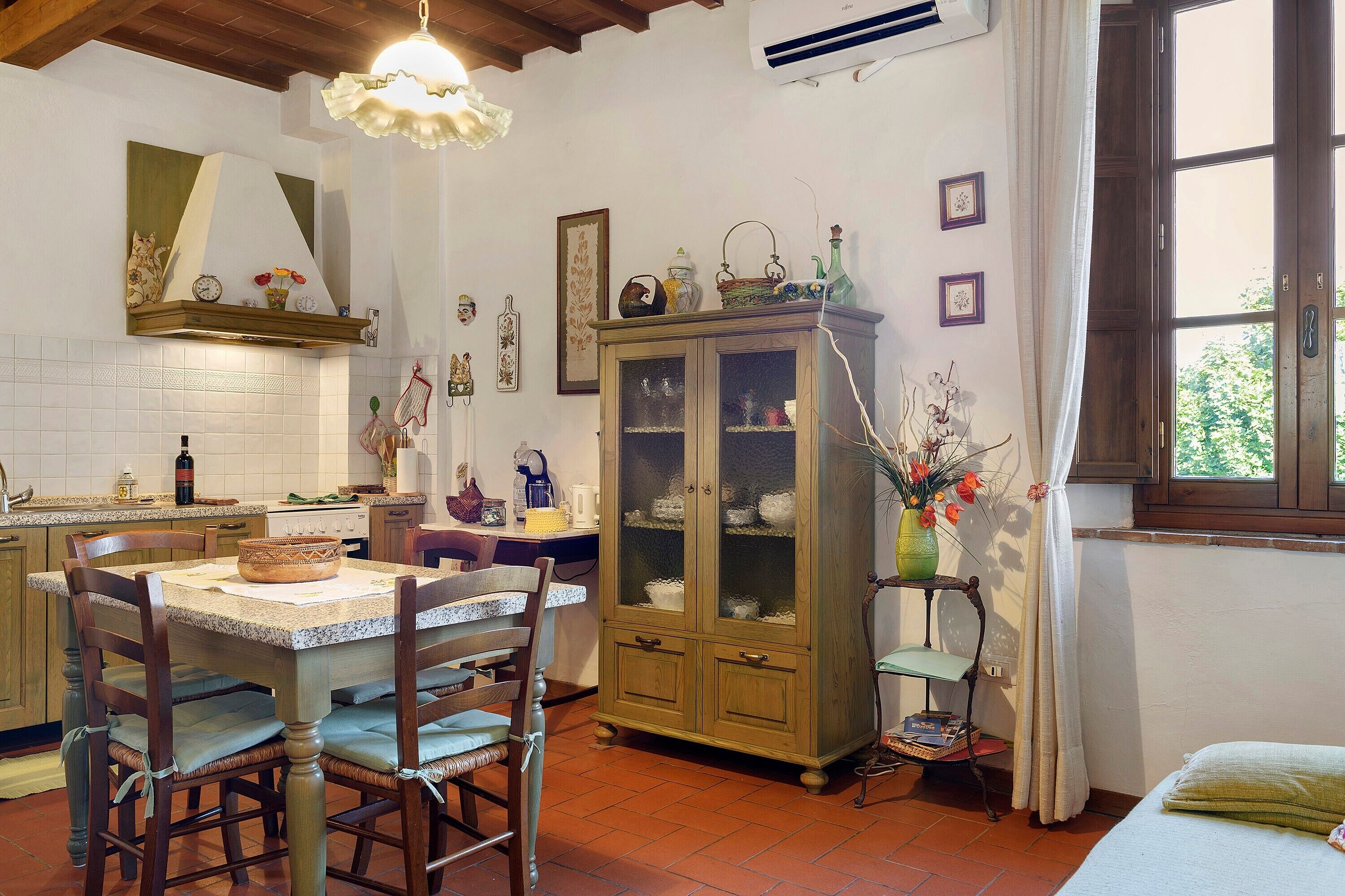 A traditional kitchen with a dining area, wooden cabinets, and a window with curtains.