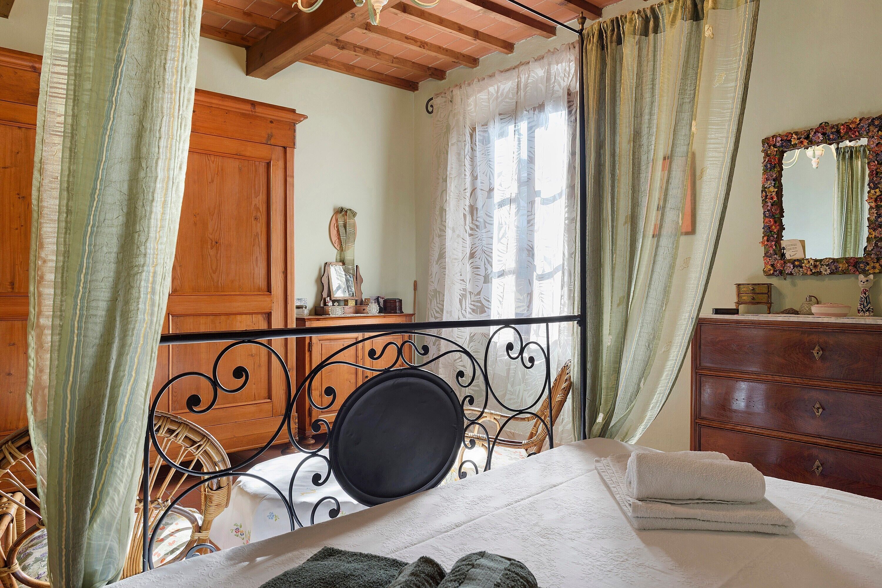 A bedroom with a bed, a dresser, a mirror, and a window with curtains.