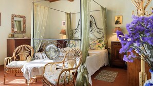 Un letto a baldacchino con tenda, un armadietto in legno, una sedia in vimini e un tavolo con tovaglia floreale.