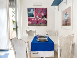 A dining area with a white table, blue tablecloth, and white chairs. There are two framed artworks on the wall. - BeHappyM • Fair/St. Ursula • Skyview (Bologna)