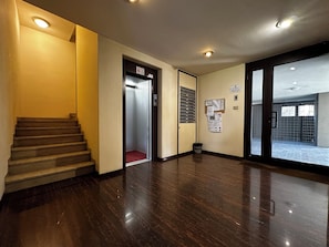 Eine Hotellobby mit Treppe, Aufzug, Mülleimer und Schwarzes Brett.