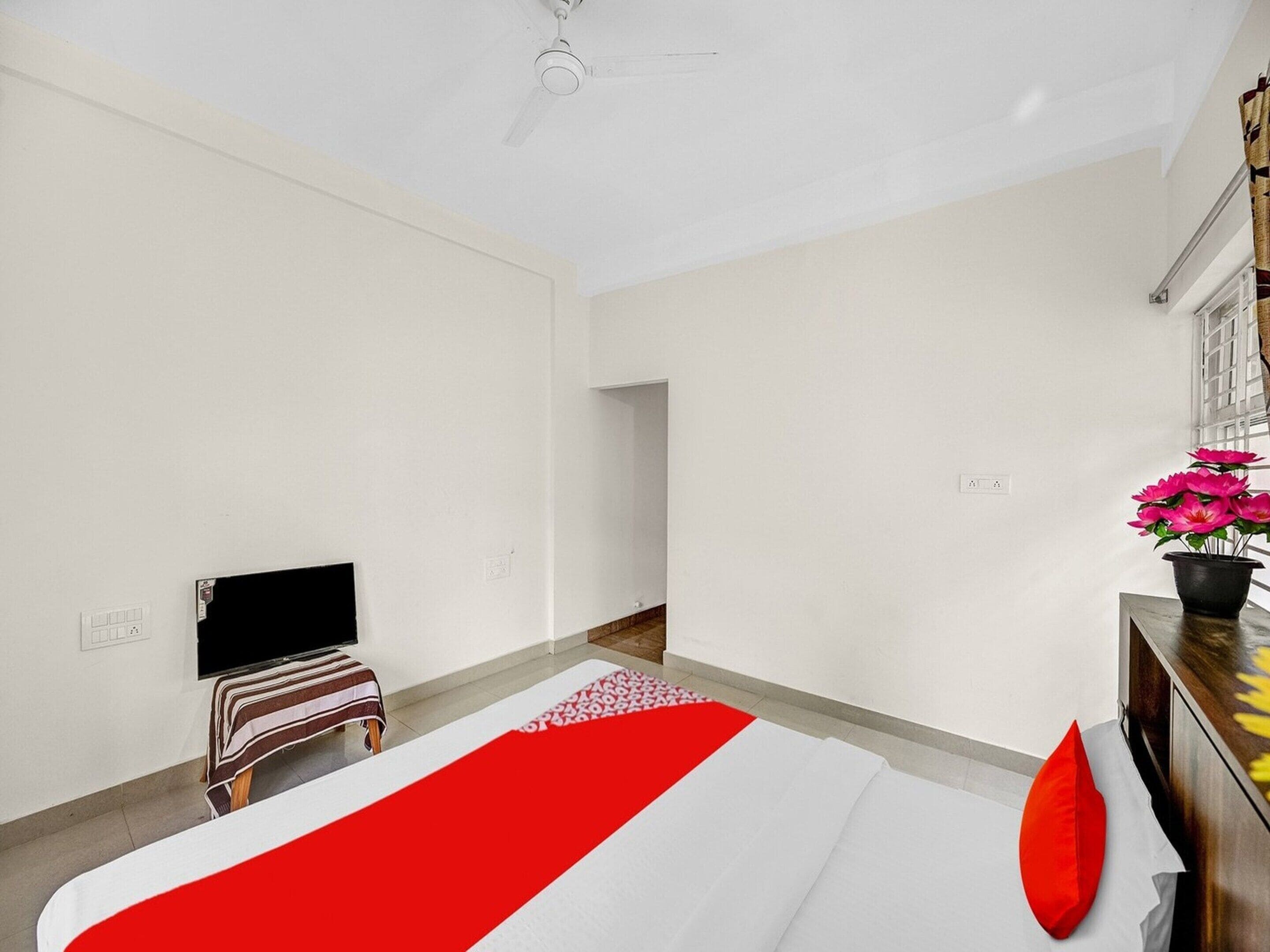 A hotel room with a bed, a TV, a small table with a plant, and a window with blinds.