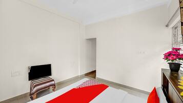 A hotel room with a bed, a TV, a small table with a plant, and a window with blinds.