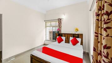 A bedroom with a bed, a window with curtains, a ceiling fan, and a bedside table with a vase of flowers.
