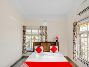 A bedroom with a bed, curtains, a window, and a bedside table. - Classic Dream Marion (Bhubaneshwar)