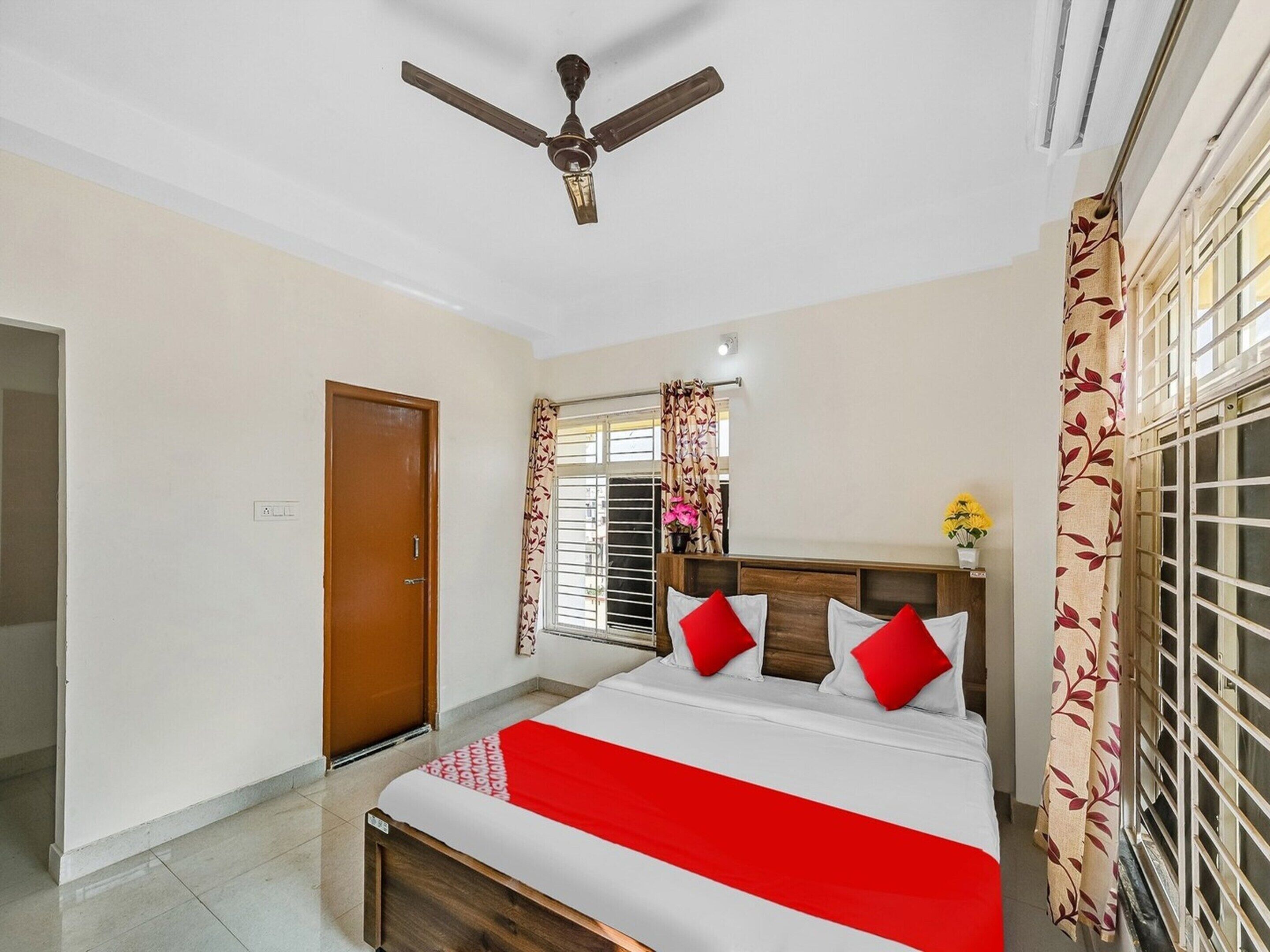 A bedroom with a bed, a ceiling fan, a window with curtains, and a door.