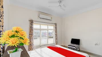 A hotel room with a bed, a TV, a ceiling fan, an air conditioning unit, and a window with curtains.