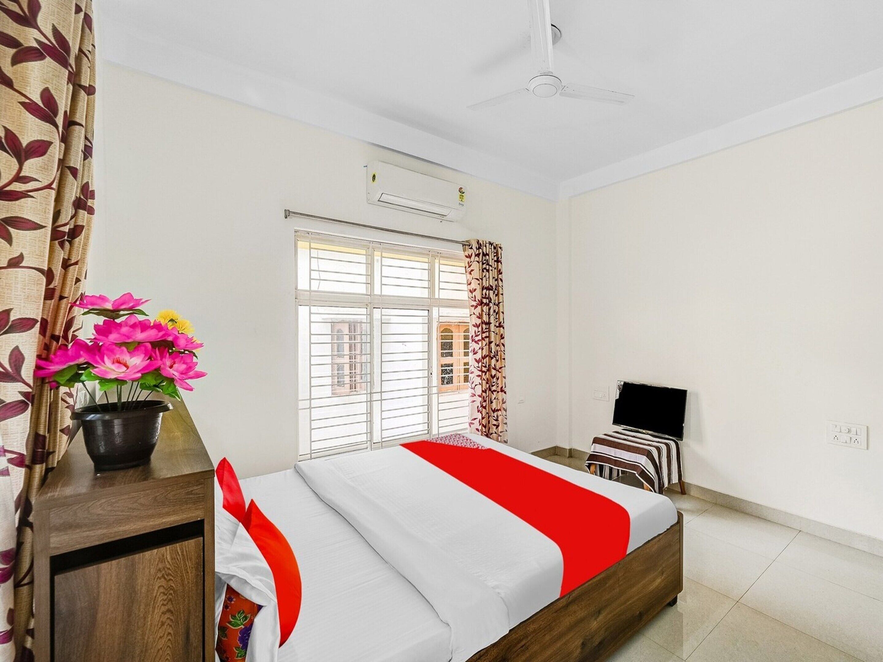 A hotel room with a bed, a TV, a window with curtains, and a ceiling fan.