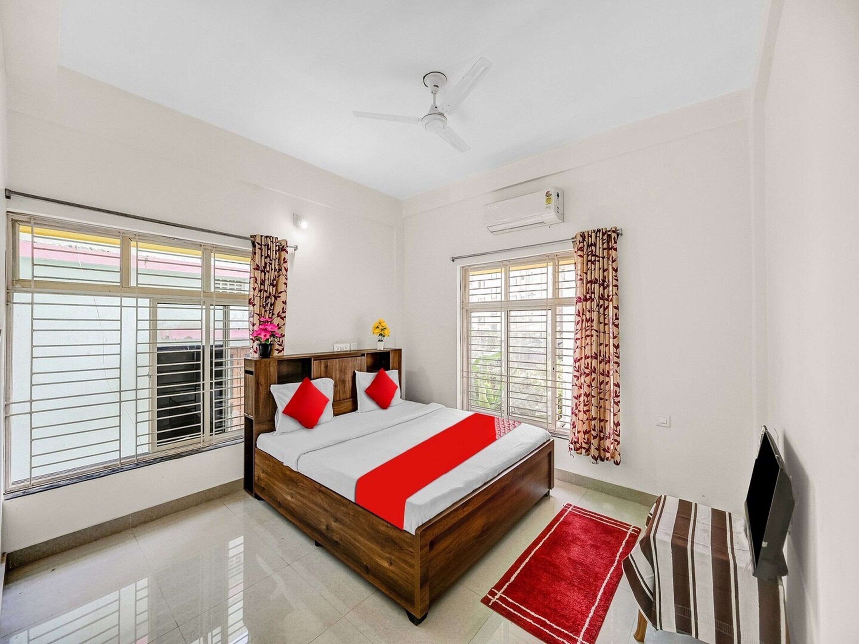 A hotel room with a bed, a ceiling fan, an air conditioning unit, and a window with curtains.