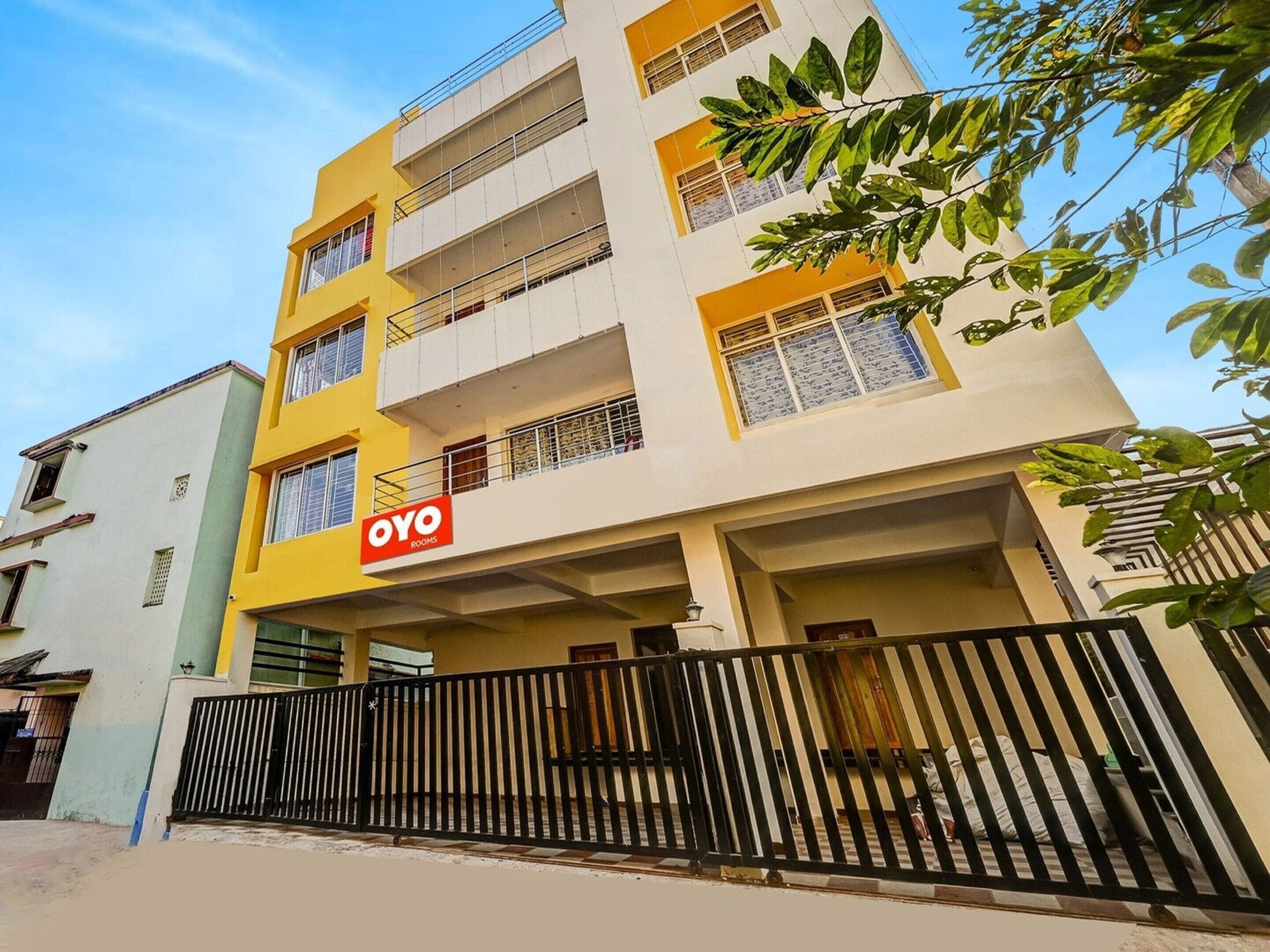 A multi-story building with a yellow and white facade, a black metal fence, and a sign for 'OYO ROOMS' indicating a hotel or lodging facility.
